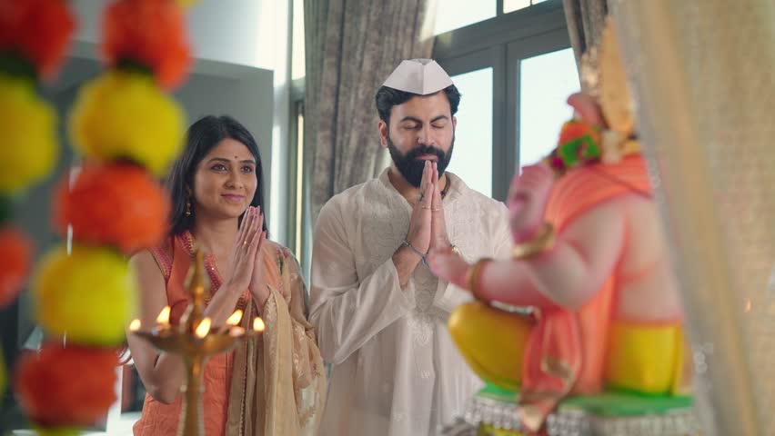 Happy ethnic Hindu Indian married couple in traditional clothes offering a prayer to a god called aarti with a Namaste posture and Marigold flowers in an indoor home. Religion, devotion, faith concept Royalty-Free Stock Footage #1098619297