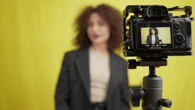 Video camera screen on the right with blurred smiling woman reflection adjusting hairdo smiling. Portrait of Caucasian social media influencer start filming vlog at yellow background