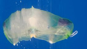 VERTICAL VIDEO, Slow motion, a plastic bag filled with plastic and other debris drifting slowly below the surface in blue water. Garbage plastic bag thrown from the ship. Close-up
