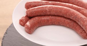  raw sausages rotate on a white plate. ready to fry. traditional cuisine. High quality 4k footage