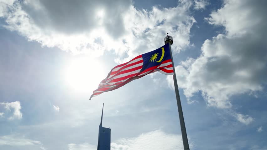 Aerial tracking Malaysia flag at Dataran Merdeka with background of PNB118 tower in blue sunny sky