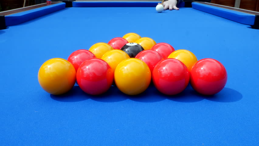Pool balls in a triange on a blue cloth pool table. The red and white balls along with the black 8 ball are hit by the white ball on the break. | Shutterstock HD Video #1098636859