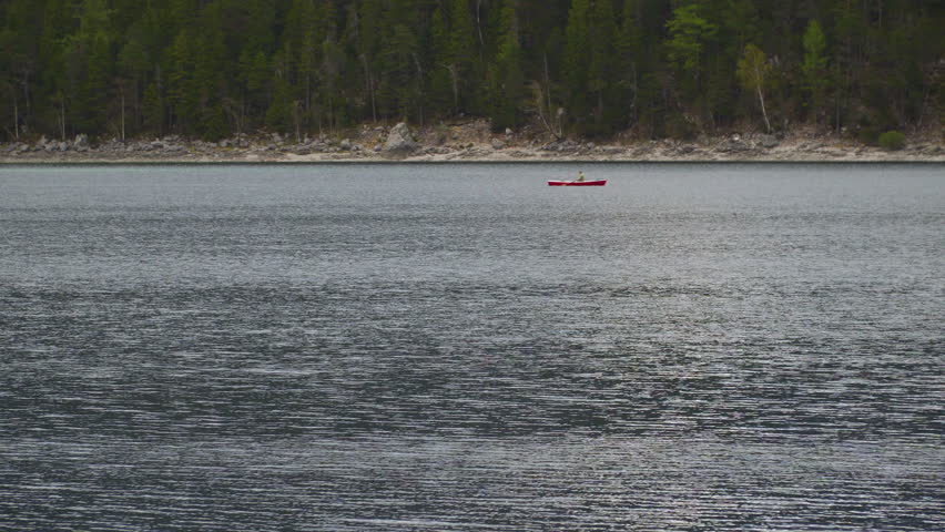 Canoe rowing across idyllic Lake Eibsee woodland shoreline in German wilderness