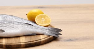 Raw fish with lemon lies on a wooden cutting board. Two fresh sea bass before cooking. 4k video.