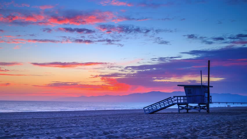 Colorful sunset over ocean in Venice Beach, Santa Monica, Los Angeles, California. Zoom in on lifeguard tower. 4K Timelapse.