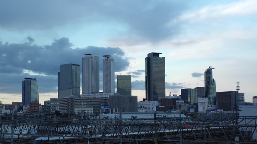 NAGOYA, JAPAN - OCT 2022 : View of buildings around NAGOYA STATION and railroad in sunset from Koyabashi (bridge). Time lapse shot, dusk to night. Japanese business and transportation concept video.