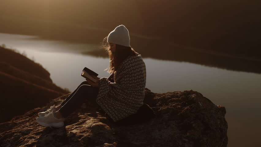 The woman opens the Bible, prays. A girl reads the Bible in the open air, studies the word of God at sunset on top of a mountain. Finding Truth in the Scriptures. Royalty-Free Stock Footage #1098646205