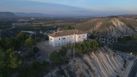 Aerial orbit video of mansion house with a traditional spanish roof tiles on the hill beside of road and the Embalse de la Pedrera reservoir. Alicante Spain