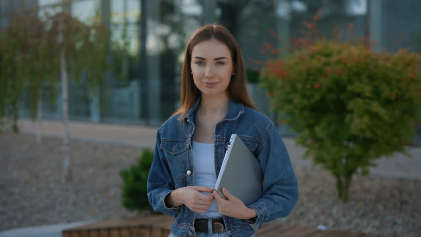 Portrait of caucasian student standing near campus holding the laptop after studying. Female professional business project manager businesswoman entrepreneur looking at the camera after work day | Shutterstock HD Video #1098654013