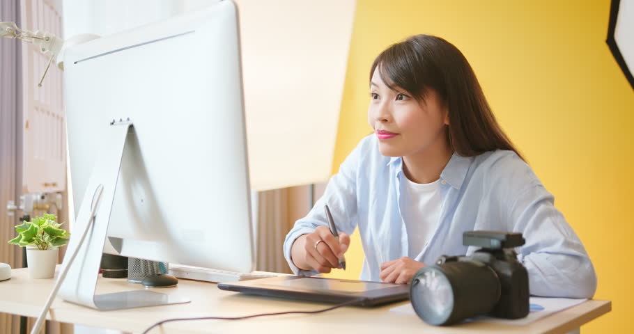 asian female photographer with digital camera is using graphics tablet and laptop computer in studio