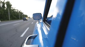 Serious male driver is reflected in left side mirror of the moving retro car. Young man driving a blue vintage auto on asphalt road. Background is defocused. Rear back view Close up Slow motion - Powered by Shutterstock - Get 15% off with code: PIKWIZARD15