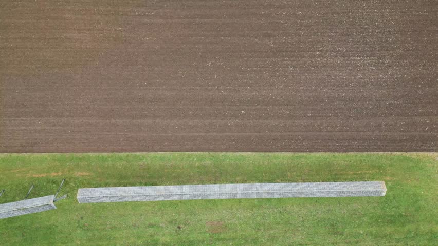 Aerial view of a hayrack standing in green meadow next to an empty field with a ploughed land.