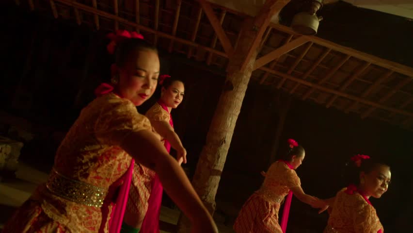 A high-angle, overhead shot captures a group of five Javanese women in traditional costumes performing a synchronized dance in a pavilion at night.