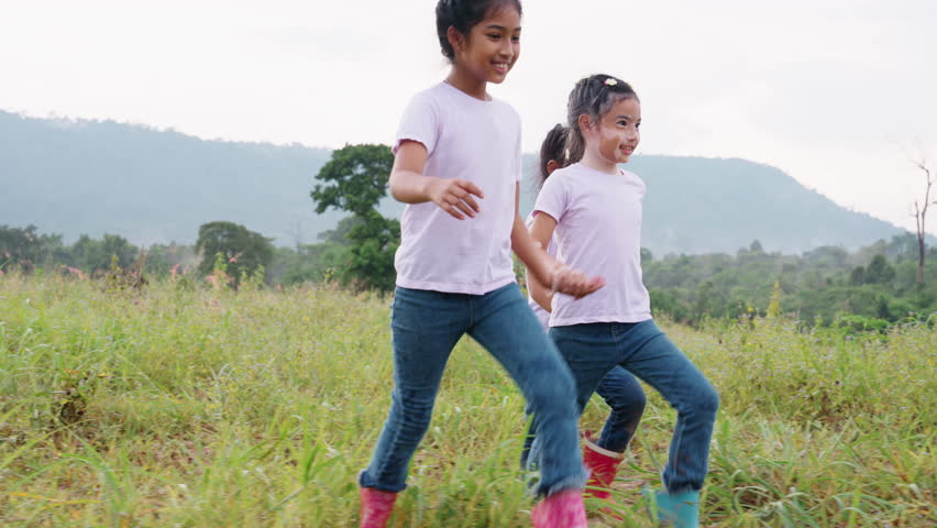 Three active sister cute child girls hold hands move way forward go walk in rural green grass field. Happy sibling young kids group asia people relax smile joy explore fun in love care nature forest. | Shutterstock HD Video #1098669651