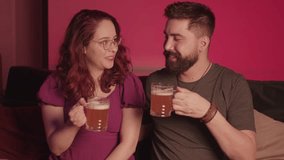 Beautiful Brazilian couple watching movies and series on TV, having a glass of beer and draft beer.