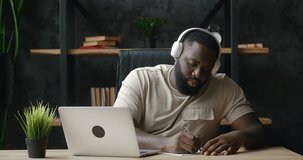 African american male in headphones studying watch foreign language class on laptop screen contact with teacher by video call take note of lesson. African student man study distantly at online courses
