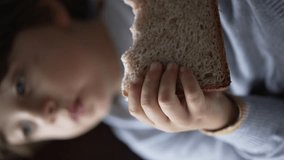 Child eating sandwich. Closeup small boy hand holding carb food snack. Kid laying on couch in Vertical Video