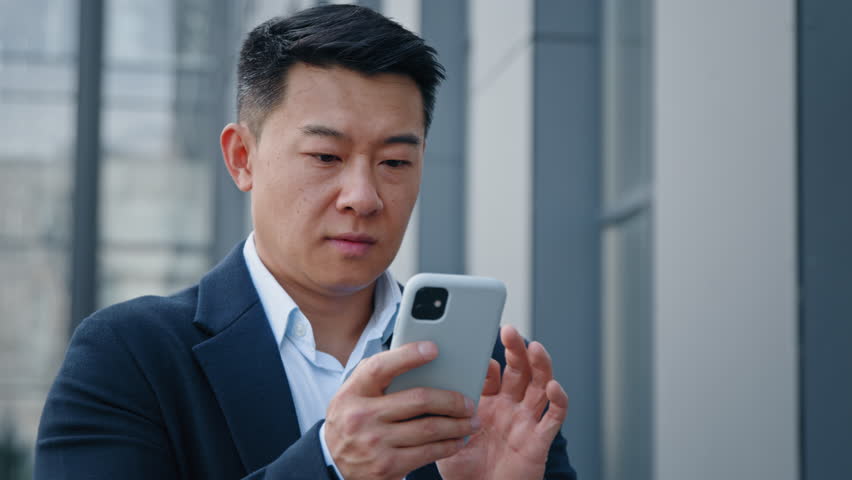 Close up Asian happy surprised man emotionally enjoys success good news 40s businessman boss win mobile online bet bid money financial prize victory receive offer opportunity on smart phone outdoors Royalty-Free Stock Footage #1098679429