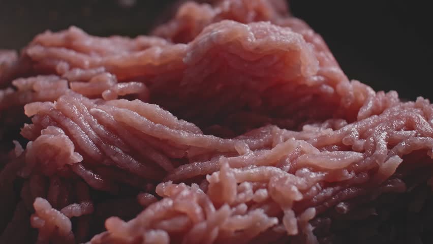 Macro shot of ground or minced meat frying in a dark nonstick frying skillet pan with seasoning sprinkled in, preparing as a filling for a Tortilla