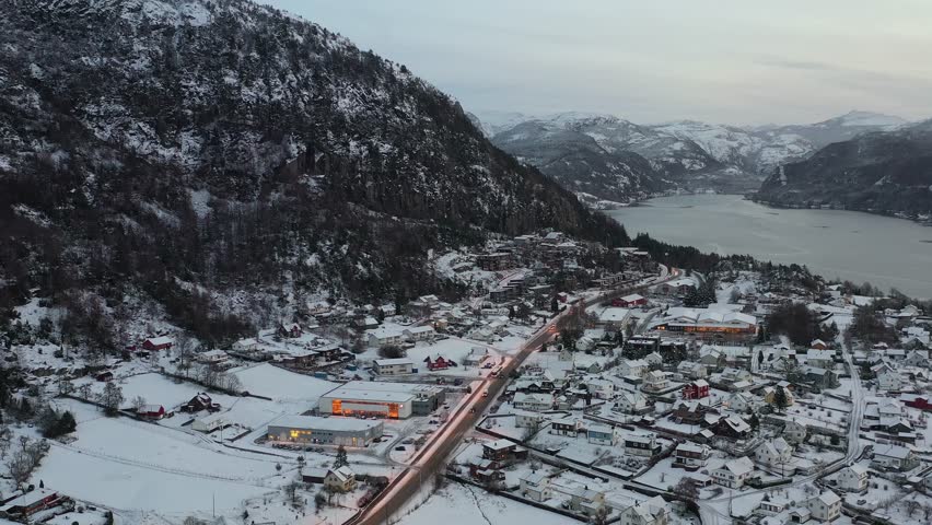 Aerial of small Norwegian town, snow covered mountains by the sea, small town with car traffic