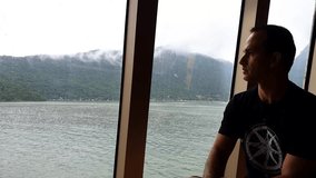 Serious 47 year old man sitting by the window of a cruise ship.