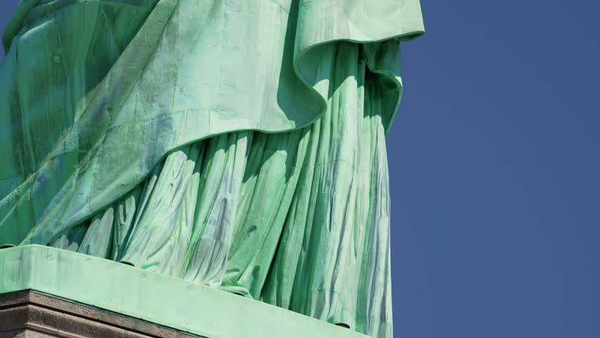 A close-up tilt shot moving upwards to reveal the whole Statue of Liberty against the clear blue sky located at Liberty Island in New York Harbor, New York City