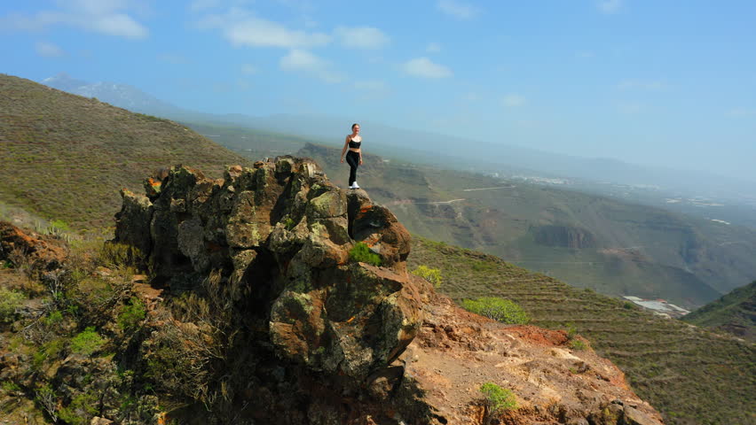 Travel to Spain. Girl enjoys hike. Young woman stands on top of mountain summit at sunset, happy and drunk on life, youth and happiness. Watching the sunset with beautiful landscape. Go everywhere.