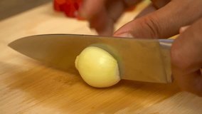 Close up of male hands cut fresh white onion on wooden cutting board on background of vegetables and greens in kitchen. Chop. Cooking food. 4k video