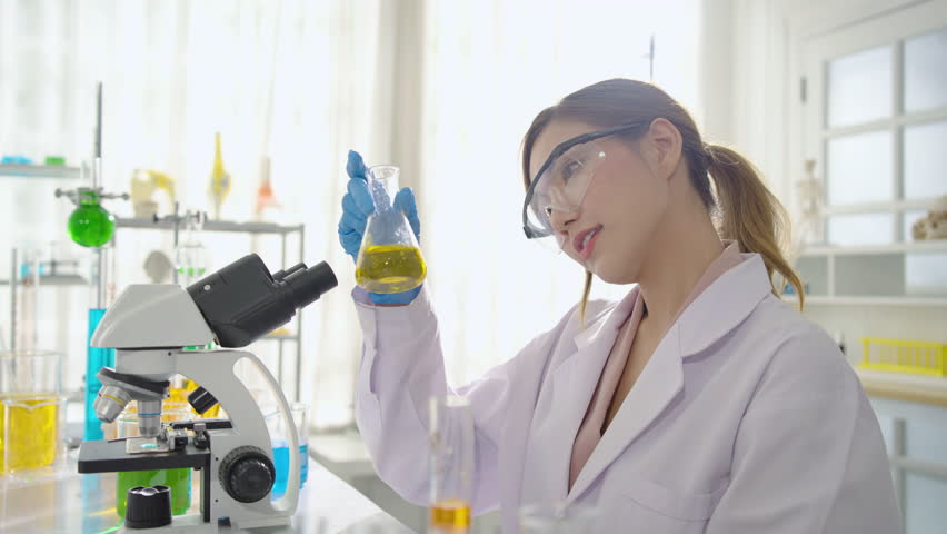 Beautiful Asian female researcher or scientist wearing sterile gloves and goggles looking and shakes a glass vial containing a special laboratory liquid. science experiment concept | Shutterstock HD Video #1098696833