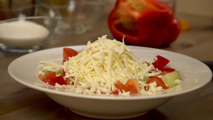 Putting the grated cheese on the salad. Fresh salad with lettuce leaves and tomato falling into bowl, served with healthy food ingredients on white table. 4k video