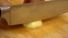 Close up of male hands cut fresh white onion on wooden cutting board on background of vegetables and greens in kitchen. Chop. Cooking food. 4k video.