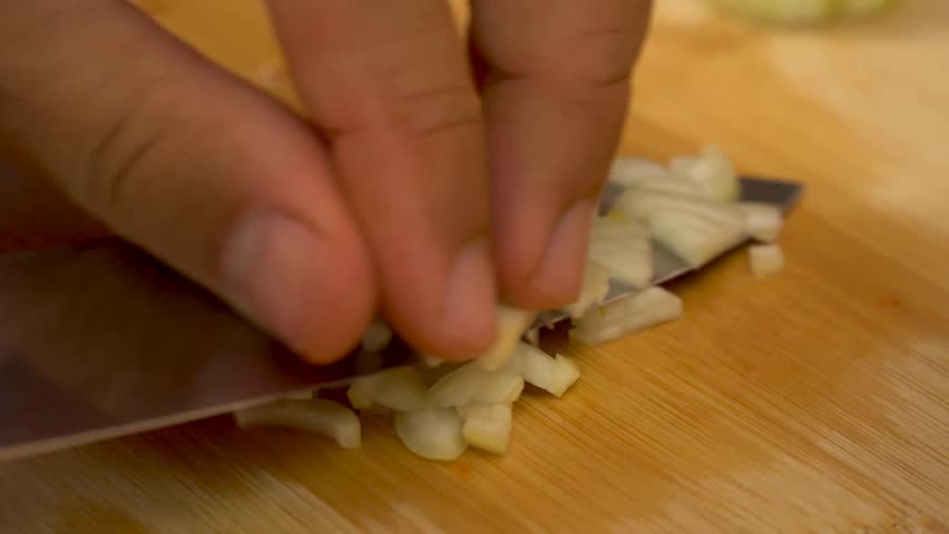 Close up of male hands cut fresh white onion on wooden cutting board on background of vegetables and greens in kitchen. Chop. Cooking food. 4k video.