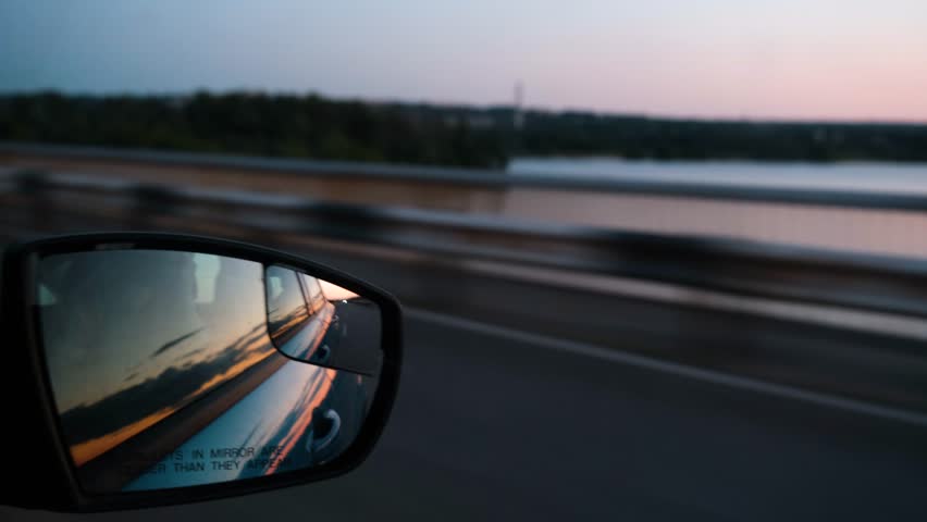View from the window of the car on the river during sunset. The car drives over the bridge over the river at sunset. Summer road trip. Autotravel