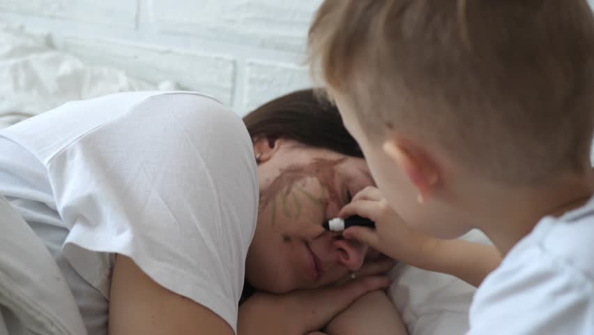 Little naughty charming boy draws markers on the face of a sleeping mom. | Shutterstock HD Video #1098702481