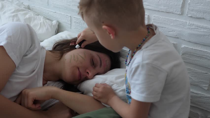 Little naughty charming boy draws markers on the face of a sleeping mom. | Shutterstock HD Video #1098702483
