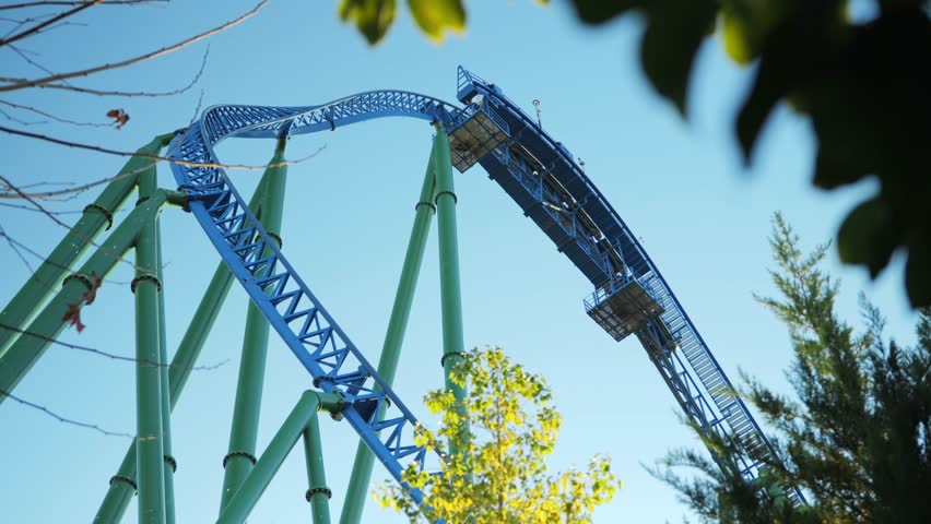 Bottom-up view from under the roller coaster, a trailer with people rides vertically down towards the camera. Vertical fall descent on a roller coaster on a clear sunny day. High quality 4k footage
