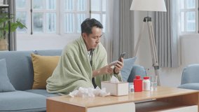Sick Asian Man With Blanket Having A Video Call With Doctor On Smartphone While Lying On Sofa In The Living Room At Home
