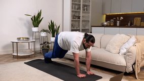 Sporty man having workout at home watching online training program. Mid adult man doing Lateral Plank Walk exercise following video tutorial on laptop indoors. Athletic guy exercising in domestic room