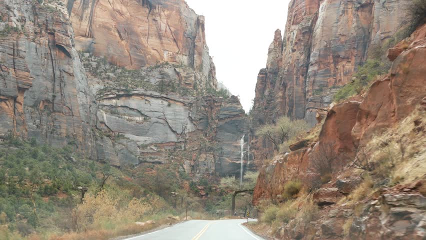 Road trip, driving auto in Zion Canyon, Utah, USA. Hitchhiking traveling in America, autumn journey. Red alien steep cliffs, rain and bare trees. Foggy weather and calm fall atmosphere. View from car.