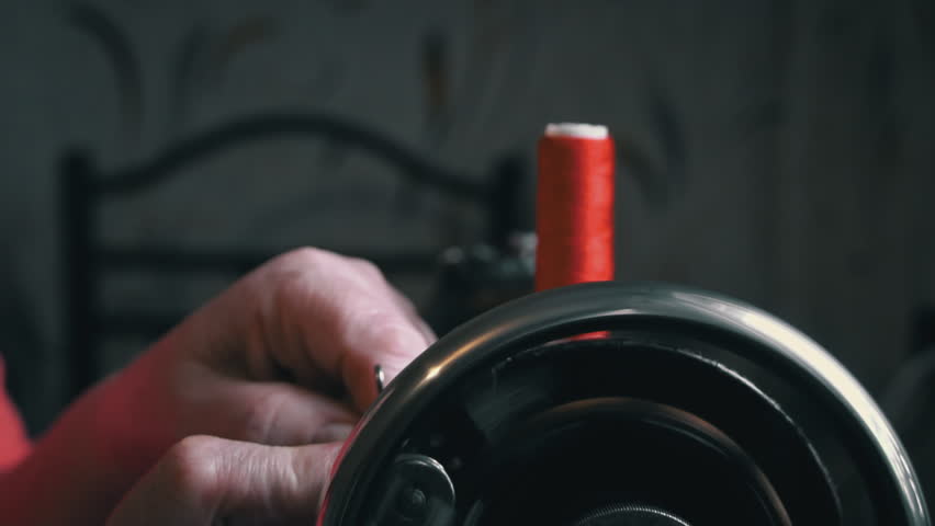 Woman winds a thread for sewing on a typewriter close-up. An elderly woman in glasses sews on an old sewing machine. A seamstress makes a machine-made even seam on a red fabric. Royalty-Free Stock Footage #1098714949