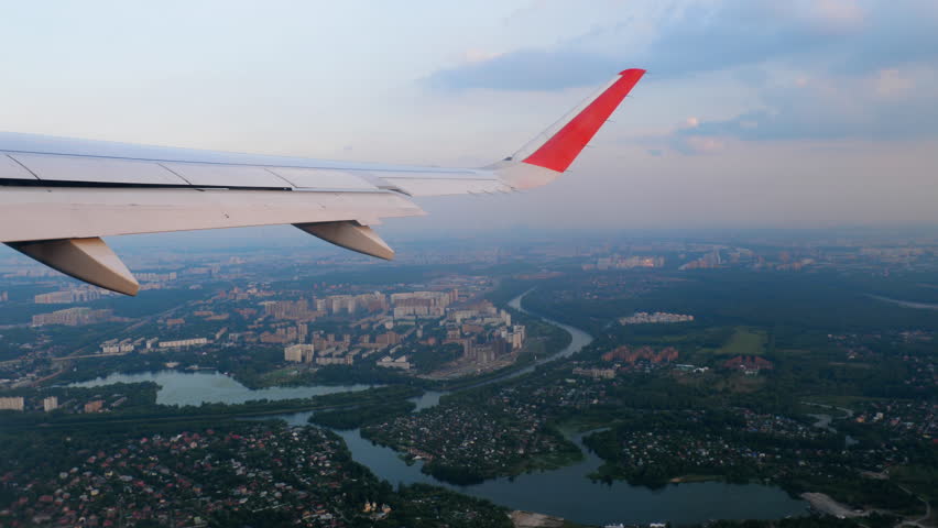 Airplane over the city, porthole. View of the wing from the window of the aircraft. Passenger plane descending for landing, POV