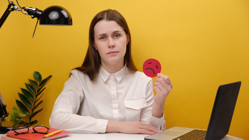 Unhappy young employee business woman in shirt sitting work at white office desk with laptop holding red sad emoticon, posing isolated over yellow color background wall in studio. Business concept | Shutterstock HD Video #1098727211