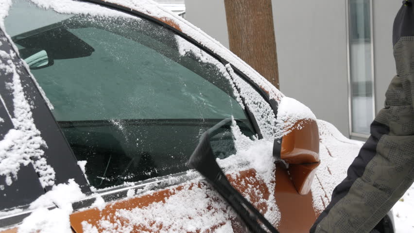 A snow-covered car covered with ice, a man with a special brush cleans the surface of the car