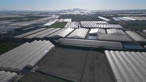 Aerial video of multiple farmers greenhouses covered by white plastic film and plowed field with a hill in a background from top down perspective. Aerial drone video top down view forward direction. - Powered by Shutterstock - Get 15% off with code: PIKWIZARD15