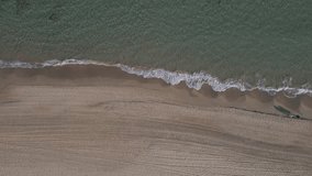 Aerial view video top-down beach on sea. Nature video view of beautiful mediterranean beach and sea at sundown. People with big shadows walking on beach.  Drone footage top down view flying Downward.