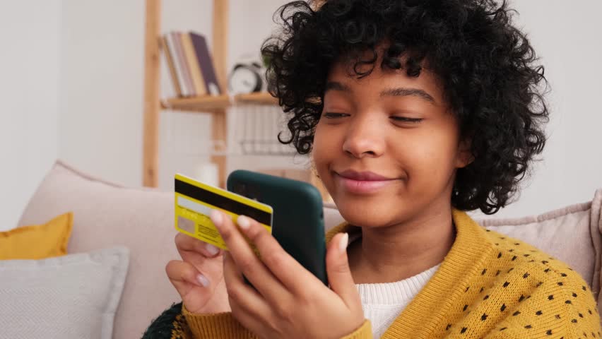 African american woman shopping online holding smartphone paying with gold credit card. Girl sitting at home buying on Internet enter credit card details. Online shopping ecommerce delivery service | Shutterstock HD Video #1098732221