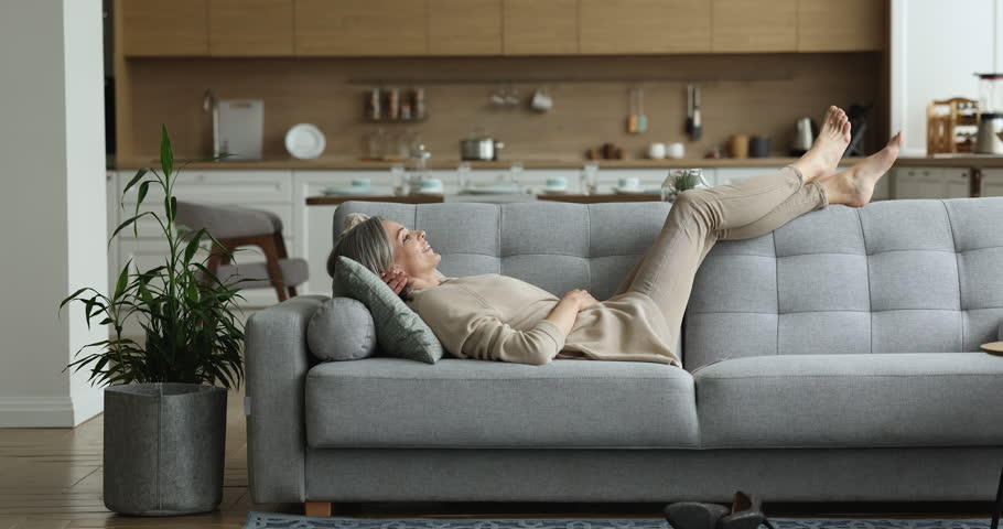 Lazy mature woman take break relaxing on cozy sofa in living room, lying on soft couch on cushion enjoy comfortable rest, breathing fresh conditioned air at home with climate control. Weekend leisure | Shutterstock HD Video #1098732525