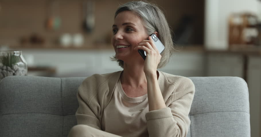 Attractive middle-aged woman relaxing on couch, blab on smartphone with friend or family, share news, lead pleasant informal conversation smile looks satisfied resting in living room. Communication Royalty-Free Stock Footage #1098732553
