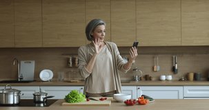 45s woman prepares salad holds cellphone record video or make videocall, stream with Internet audience showing lettuce ingredient for healthy dietary dish standing in kitchen. Communication, food vlog
