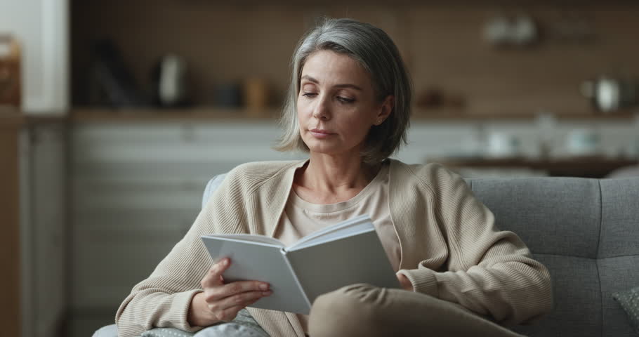 Beautiful middle-aged 45s woman relaxing holds reading book resting on cozy sofa, smile enjoy leisure, carefree weekend with favourite literature and home pastime. Good life habit, development, hobby Royalty-Free Stock Footage #1098732637